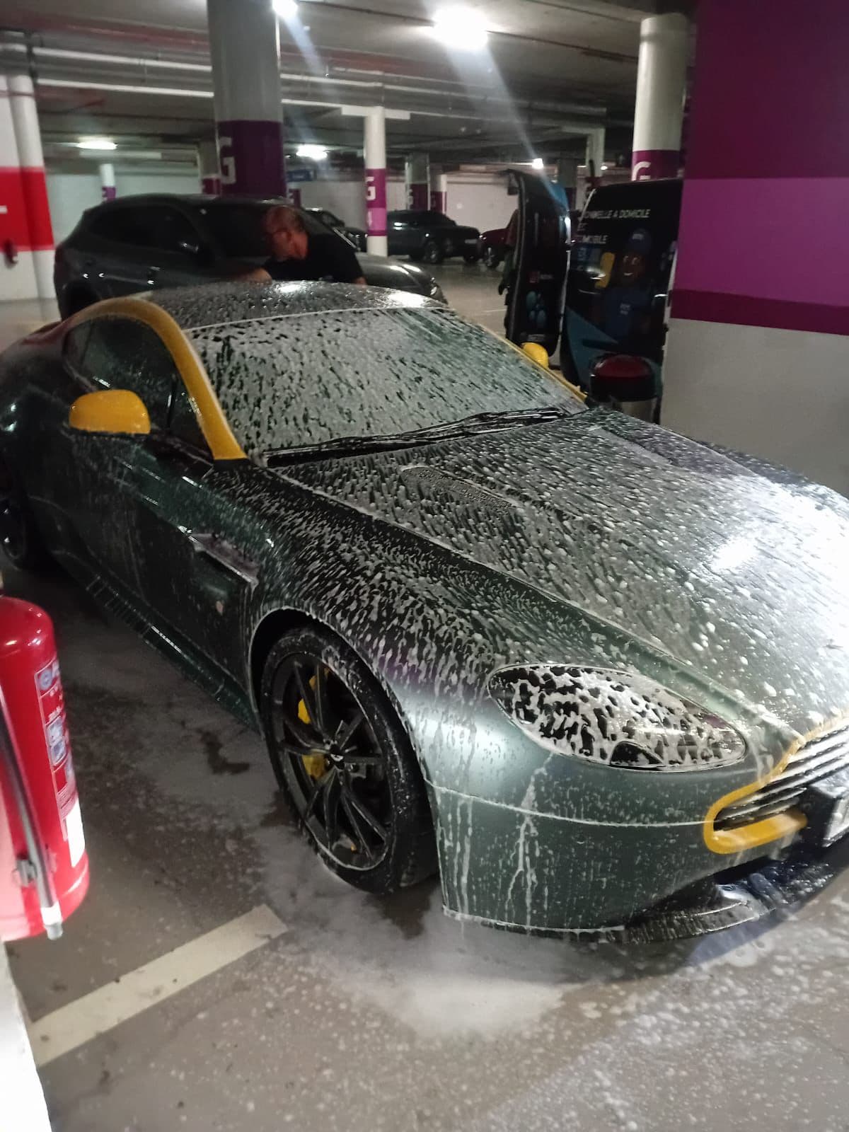 Green Aston Martin with yellow accents covered in soap suds in a parking garage.