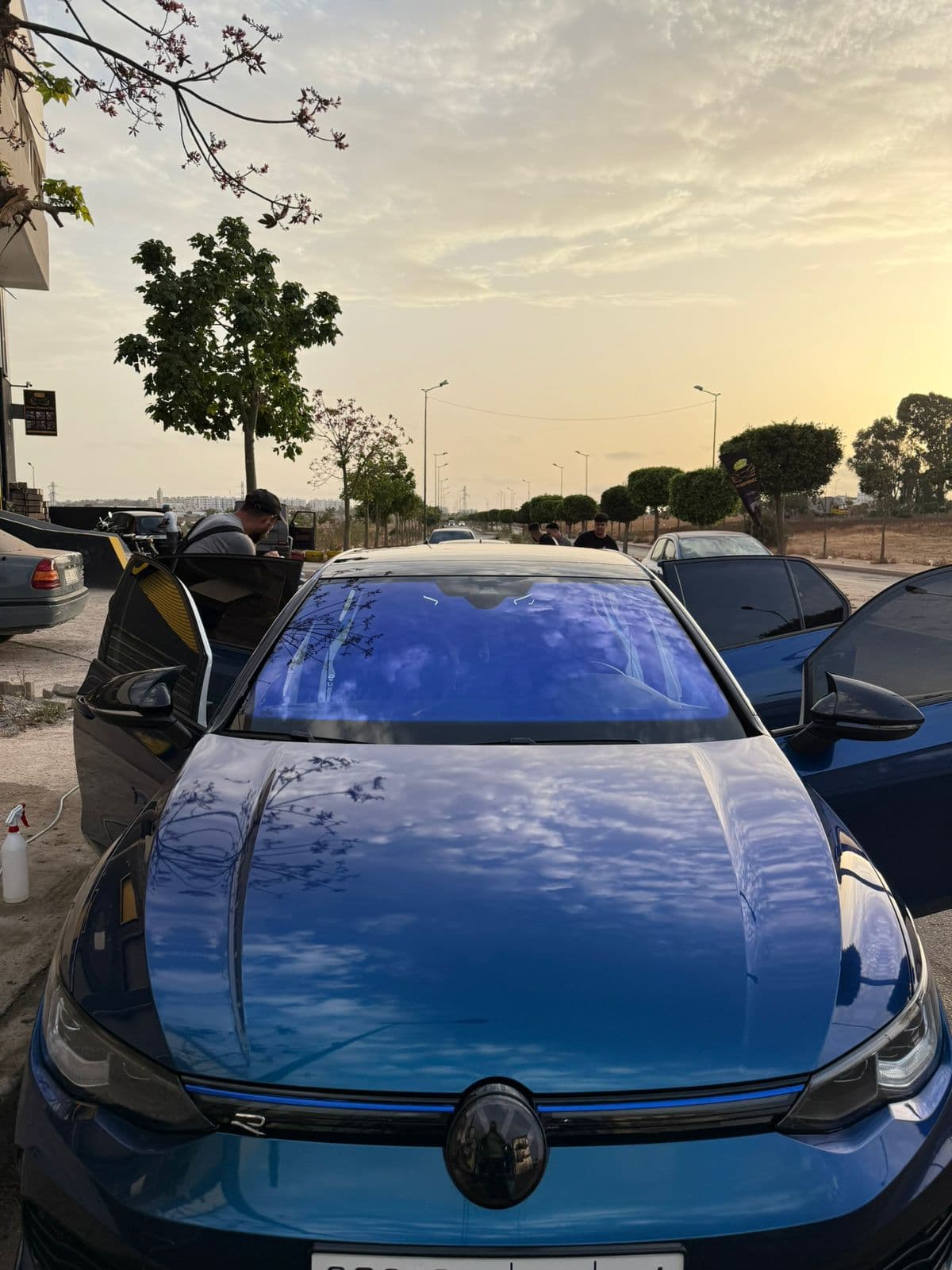 Blue Volkswagen Golf R with open doors, reflecting a bright cloudy sky on the hood.