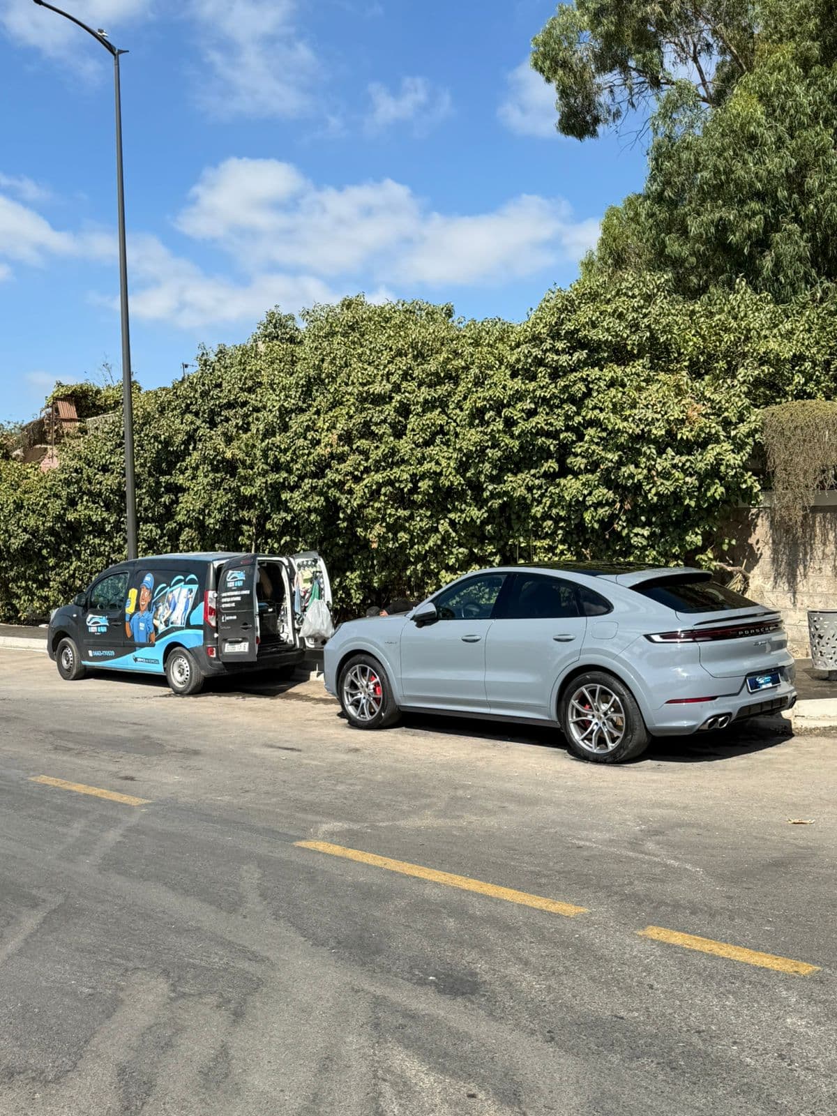Grey Porsche Cayenne Coupe parked on a street behind a mobile car detailing van.