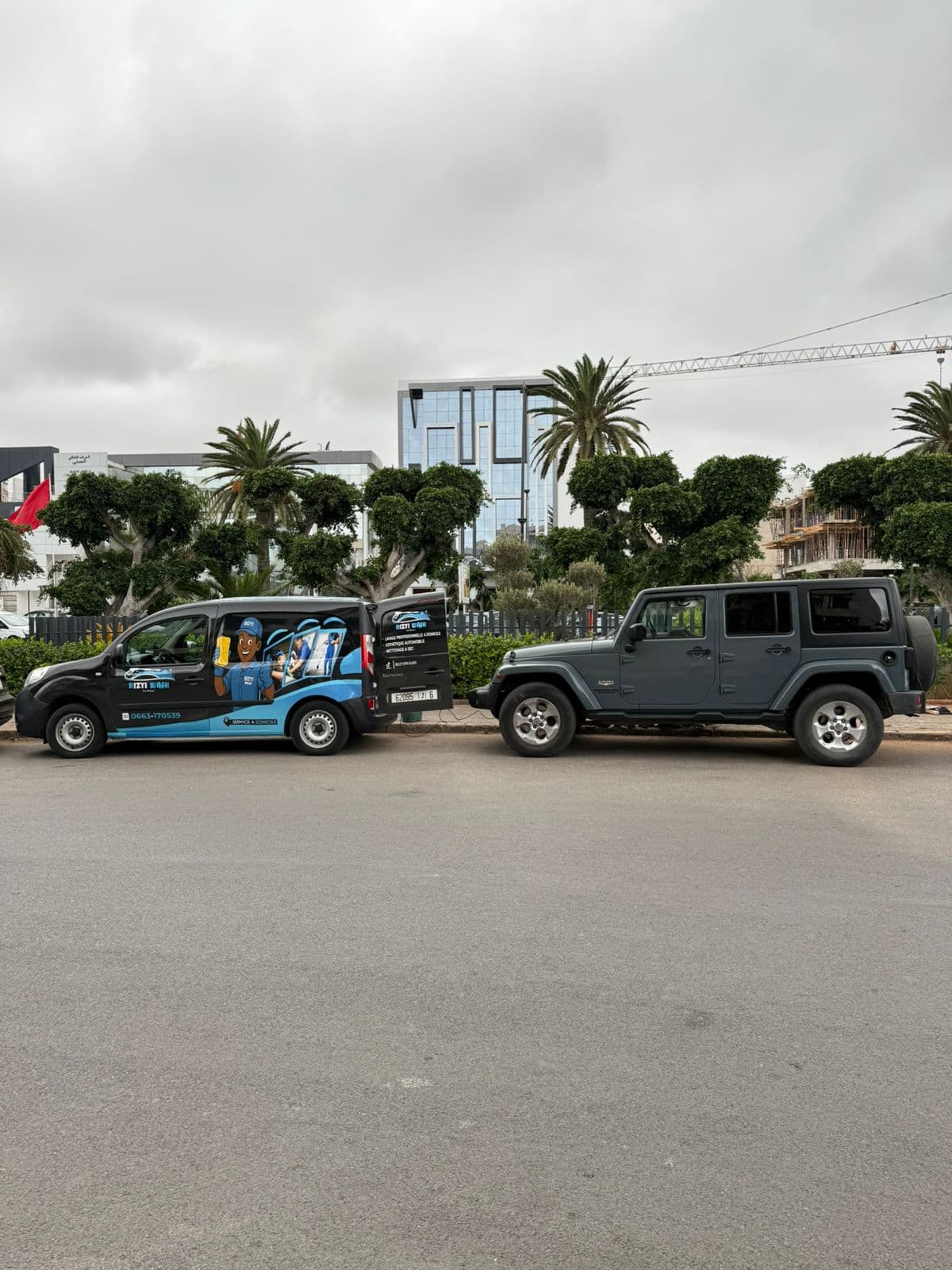 Branded mobile car wash van parked behind a grey Jeep Wrangler on a city street.