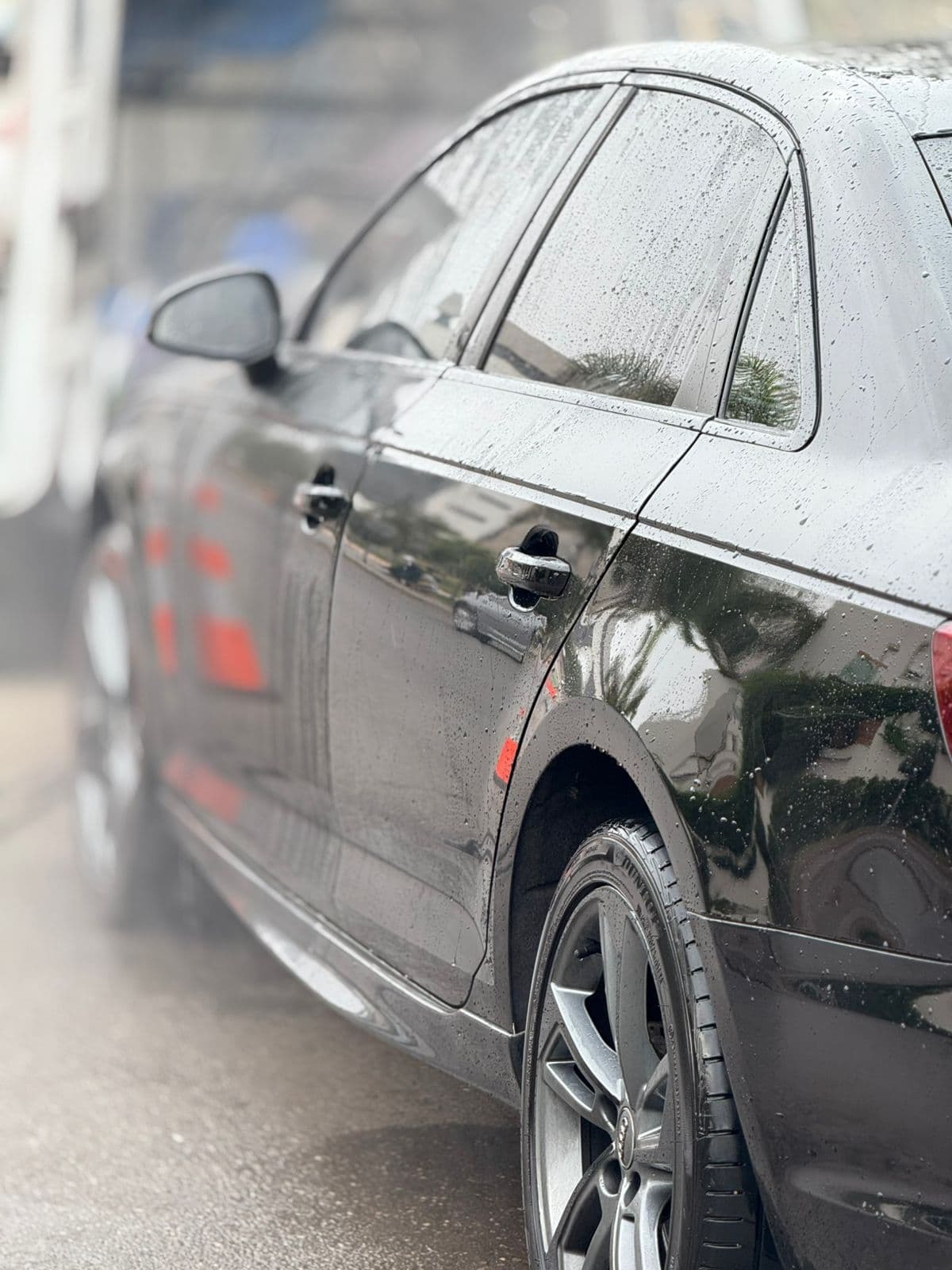 Side view of a wet black car with raindrops glistening on its shiny paint.