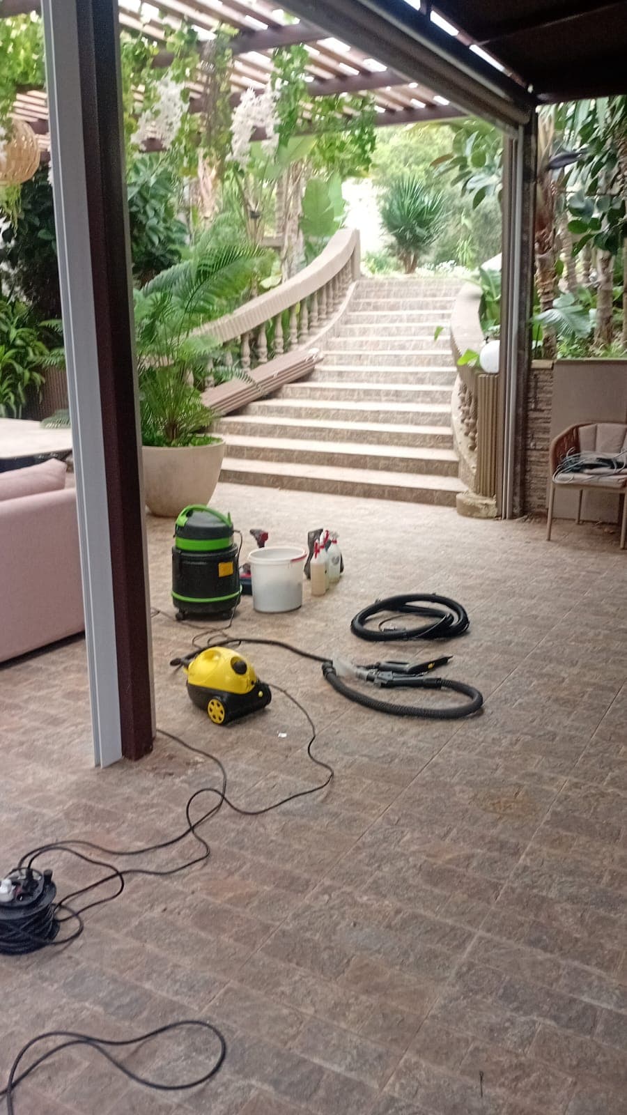 Cleaning equipment on a tiled patio overlooking a stone staircase and lush tropical garden.