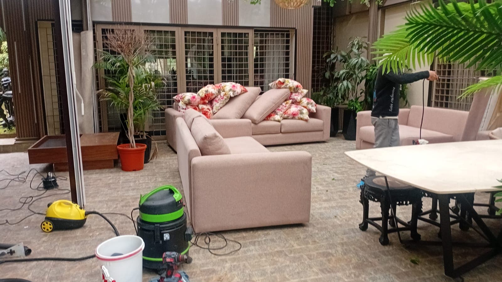Professional cleaning of pink sofas on a patio with vacuums, floral cushions, and greenery.