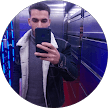 Man in a shearling jacket takes a mirror selfie inside a blue-lit elevator.